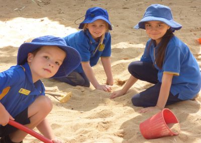 Three children playing in the sand pit while posing for the camera